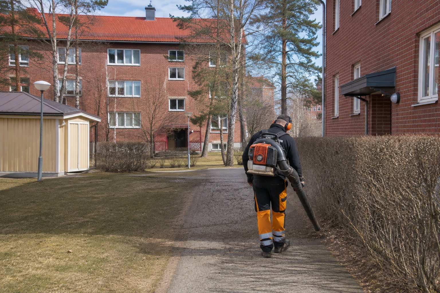 Fastighetsskötare sedd bakifrån arbetar i ett svenskt bostadsområde